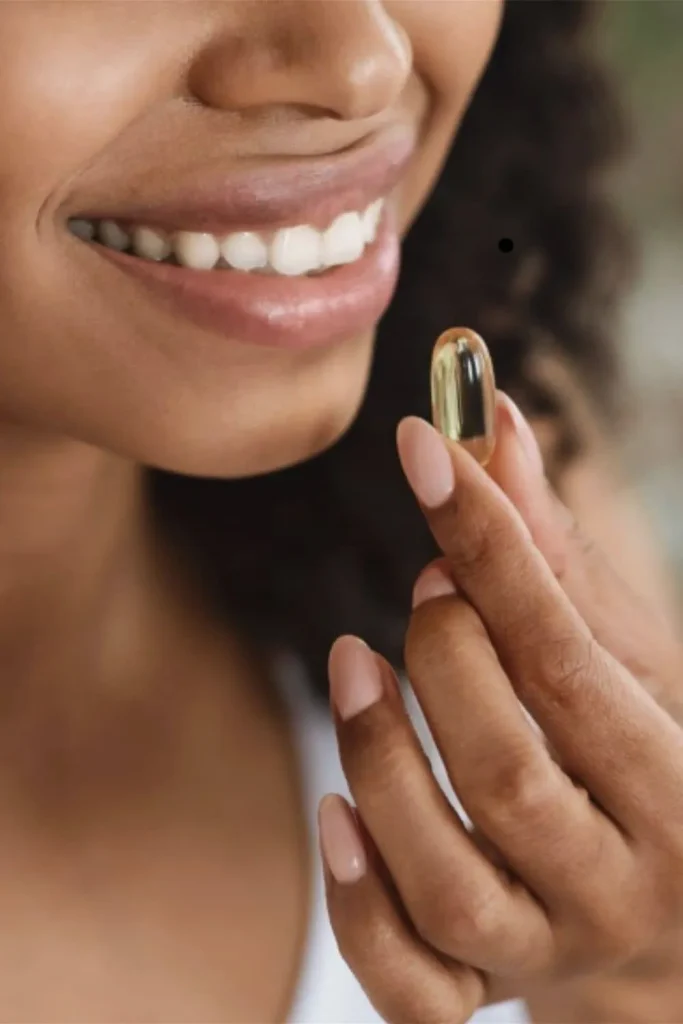 A woman holding a vitamin capsule to her lips to illustrate the role of supplements in how to grow nails fast.