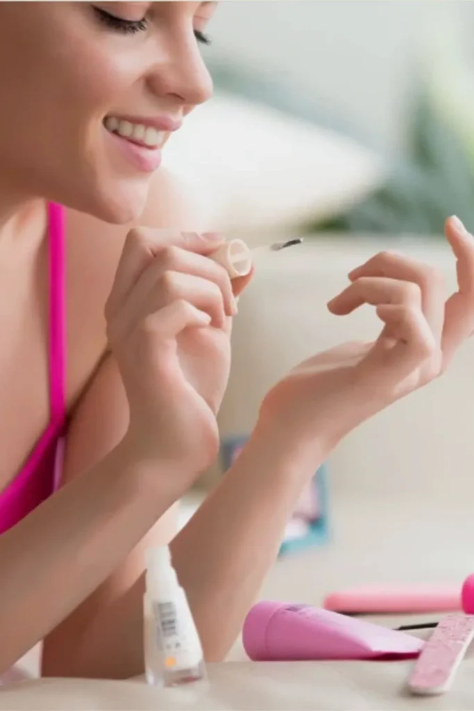 A woman applying a clear strengthening base coat to her natural nails to show how to grow nails fast by protecting them from breakage.